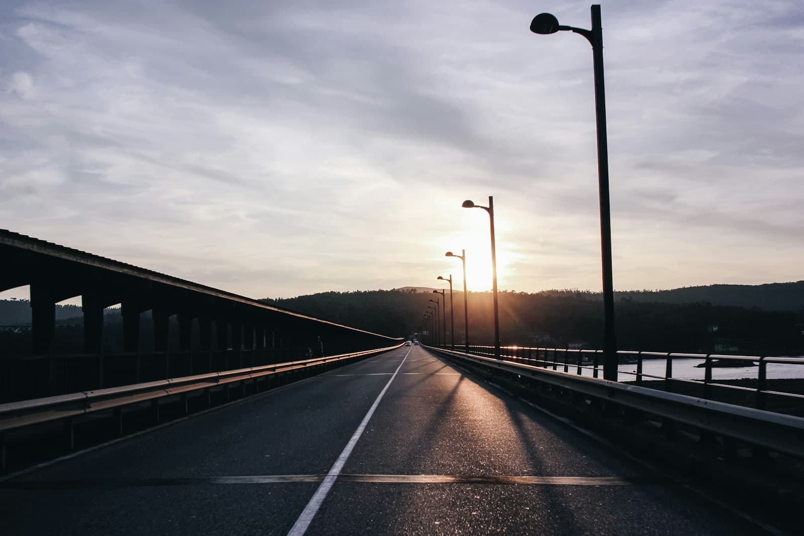 An empty road crossing a long bridge at sunset